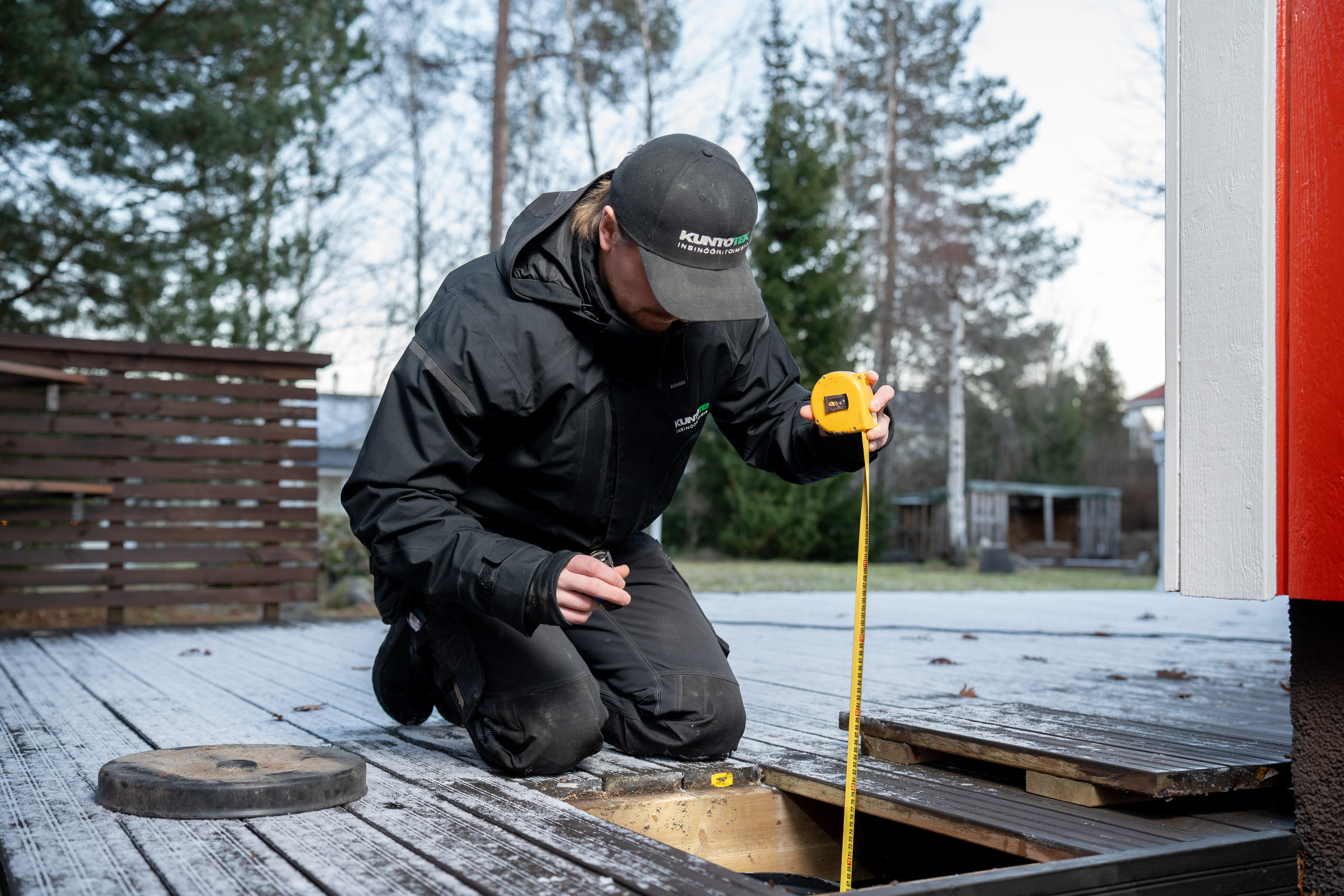 Kuntotarkastaja suorittaa rakenteiden tarkastusmittauksia rullamitalla ulkoterassin äärellä. 