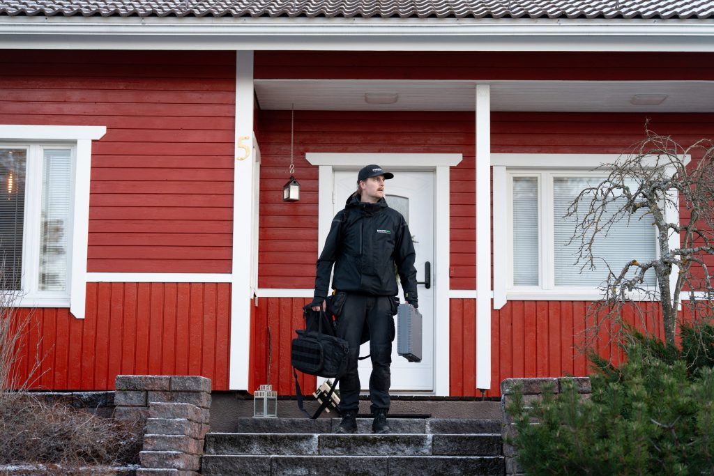 Kuntotarkastaja suorittamassa omakotitalon julkisivun ja rakenteiden tarkastusta. Kuntotek Oy:n asiantuntija arvioimassa puuverhoillun talon kuntoa ammattilaisten varusteilla.