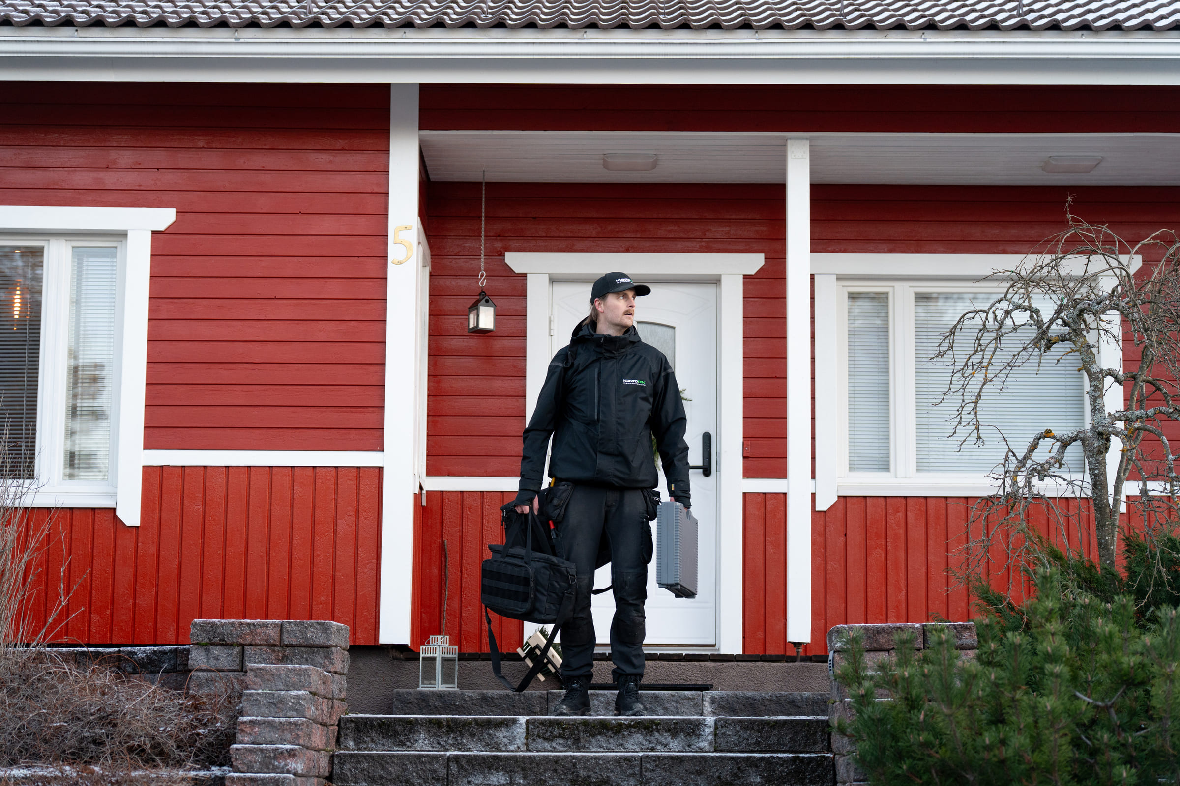 Kuntotarkastaja suorittamassa omakotitalon julkisivun ja rakenteiden tarkastusta. Kuntotek Oy:n asiantuntija arvioimassa puuverhoillun talon kuntoa ammattilaisten varusteilla.